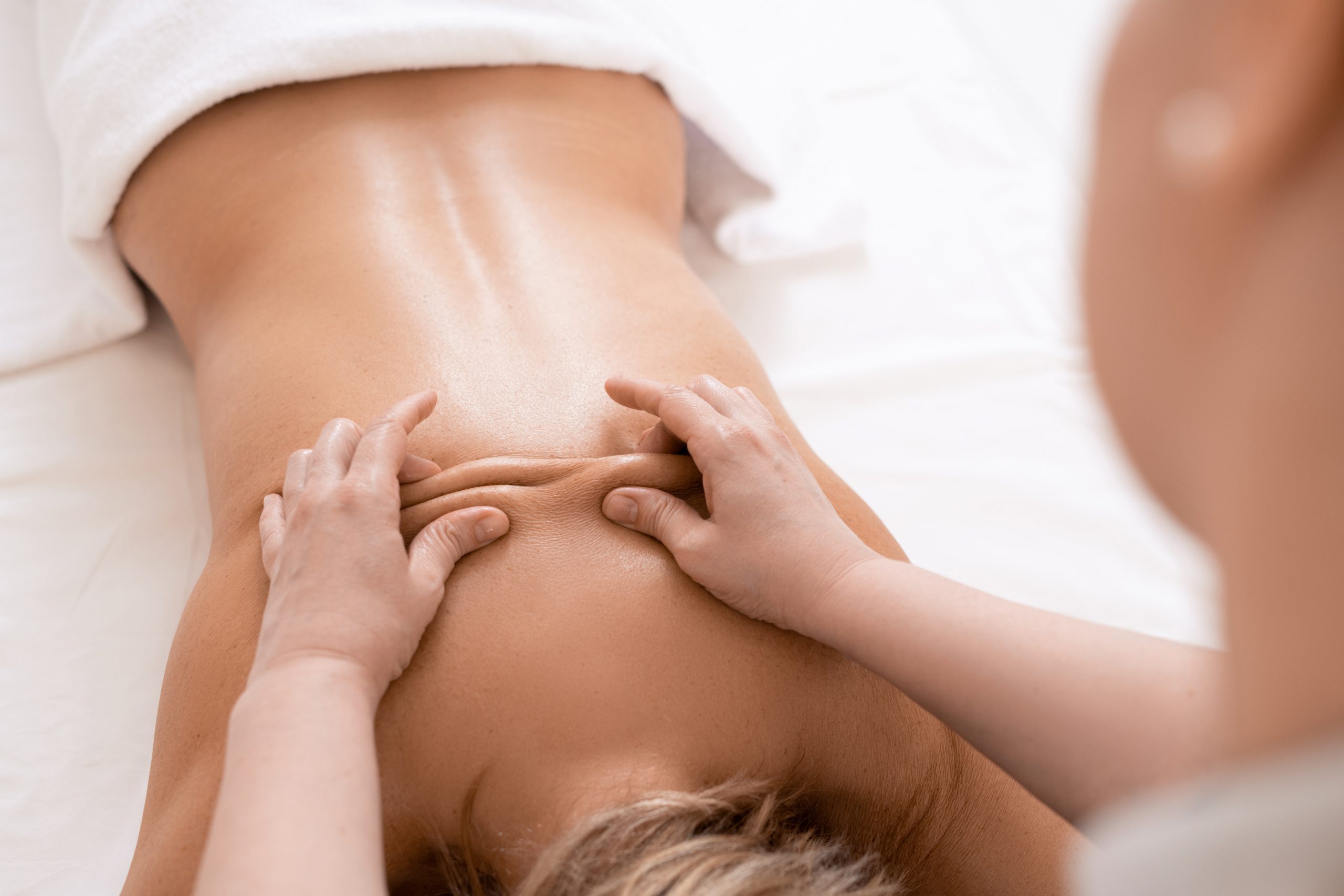 Over shoulder view of masseur performing deep tissue massage of womens back to release pain